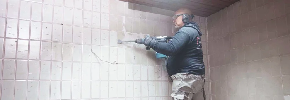 Person entfernt Fliesen mit Bohrhammer